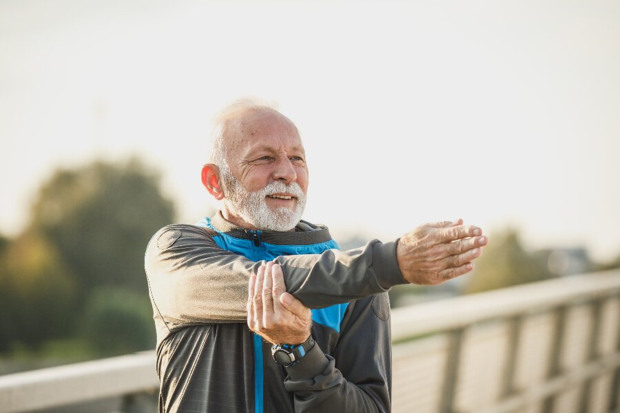 An older man stretching his arms outdoors