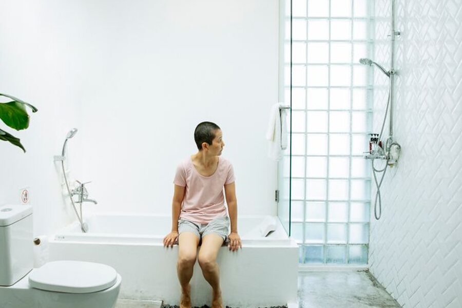 A person sitting on the edge of a bathtub in a bright bathroom